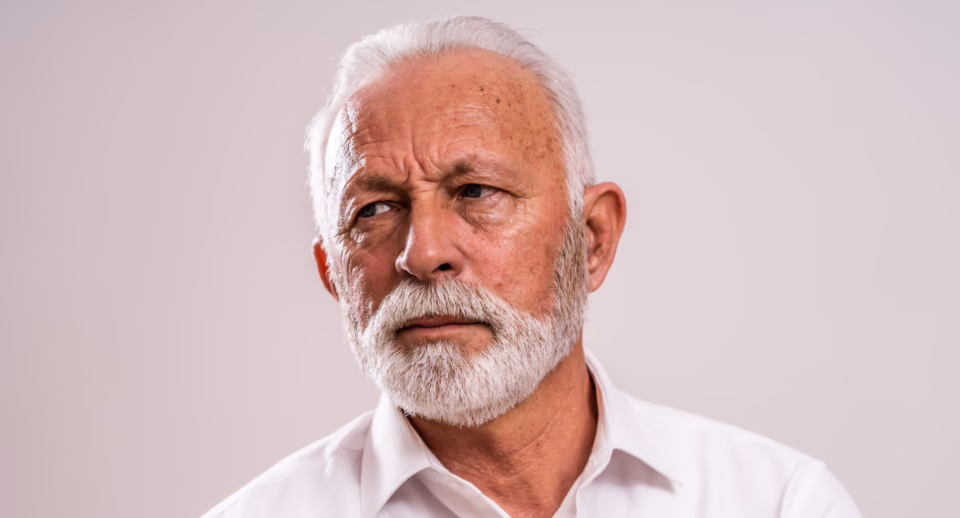 A senior man with a serious expression and hooded eyelids